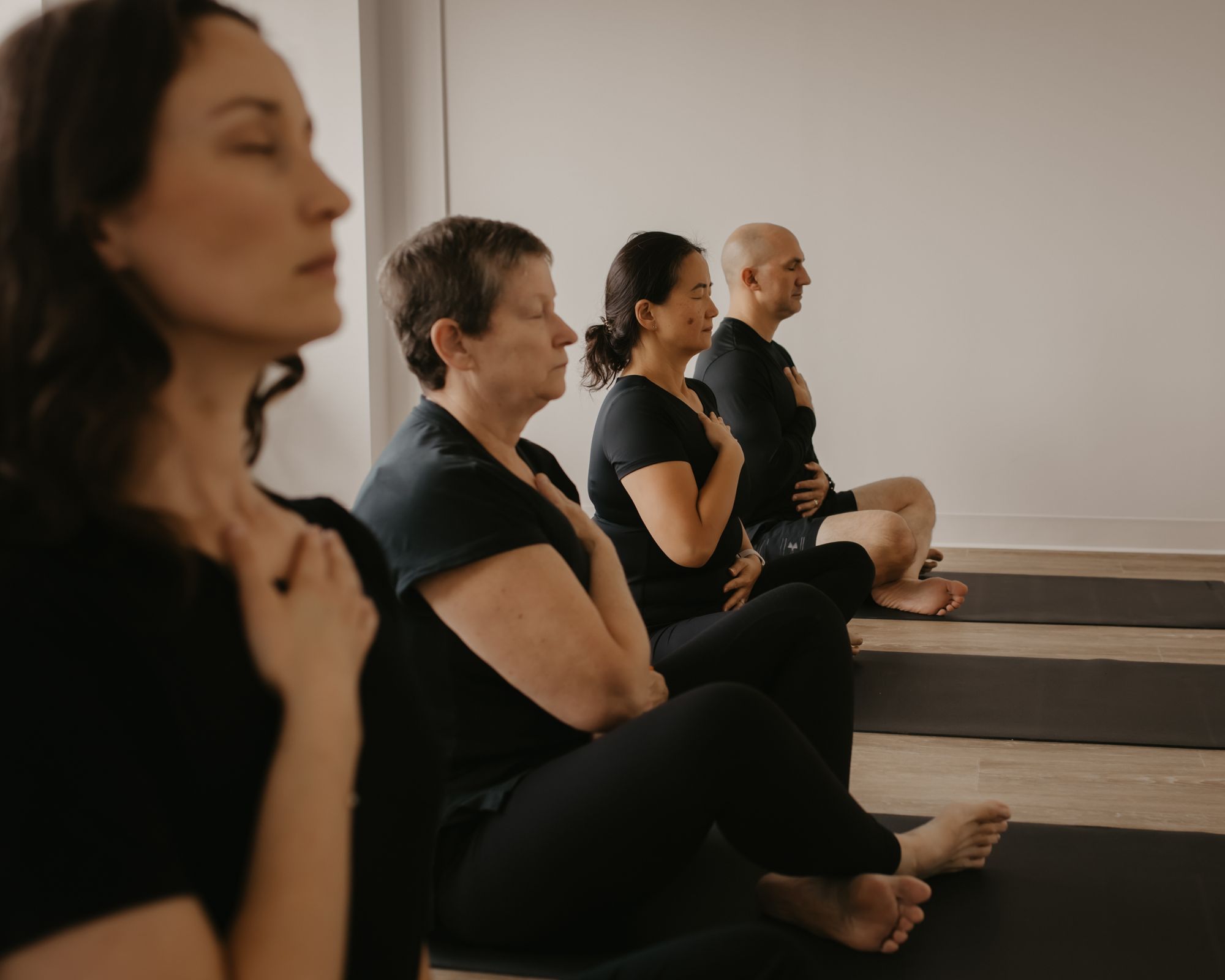 Practitioners seated on mats with eyes closed and hands on their chests during a breath practice
