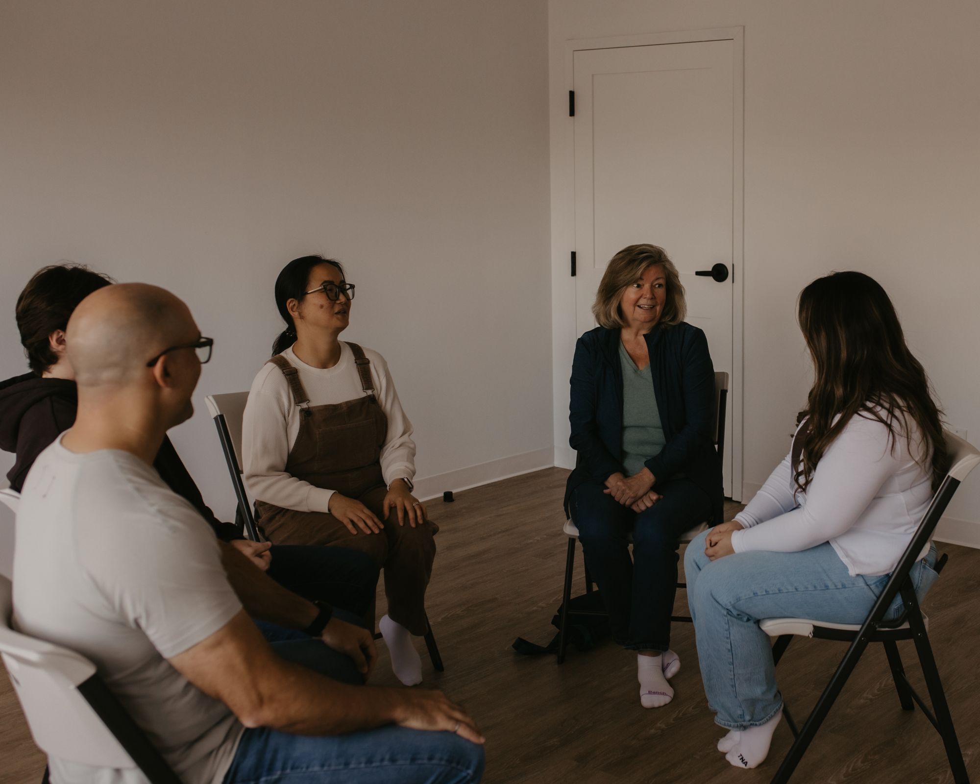 A group of practitioners seated in a circle, talking together in a bright room